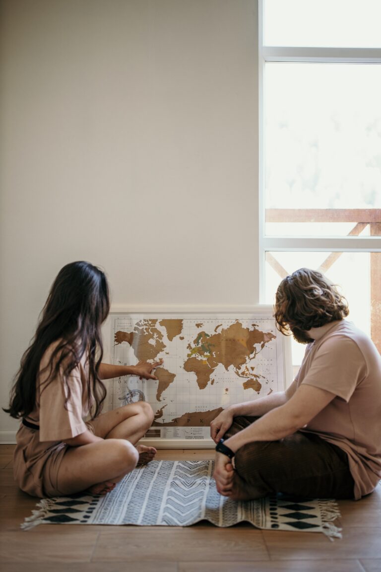 Une femme assise par terre, montrant un pays sur une planisphère, à un homme assis par terre à côté d'elle, tous les deux sont de profil, tête tournée vers le mur.